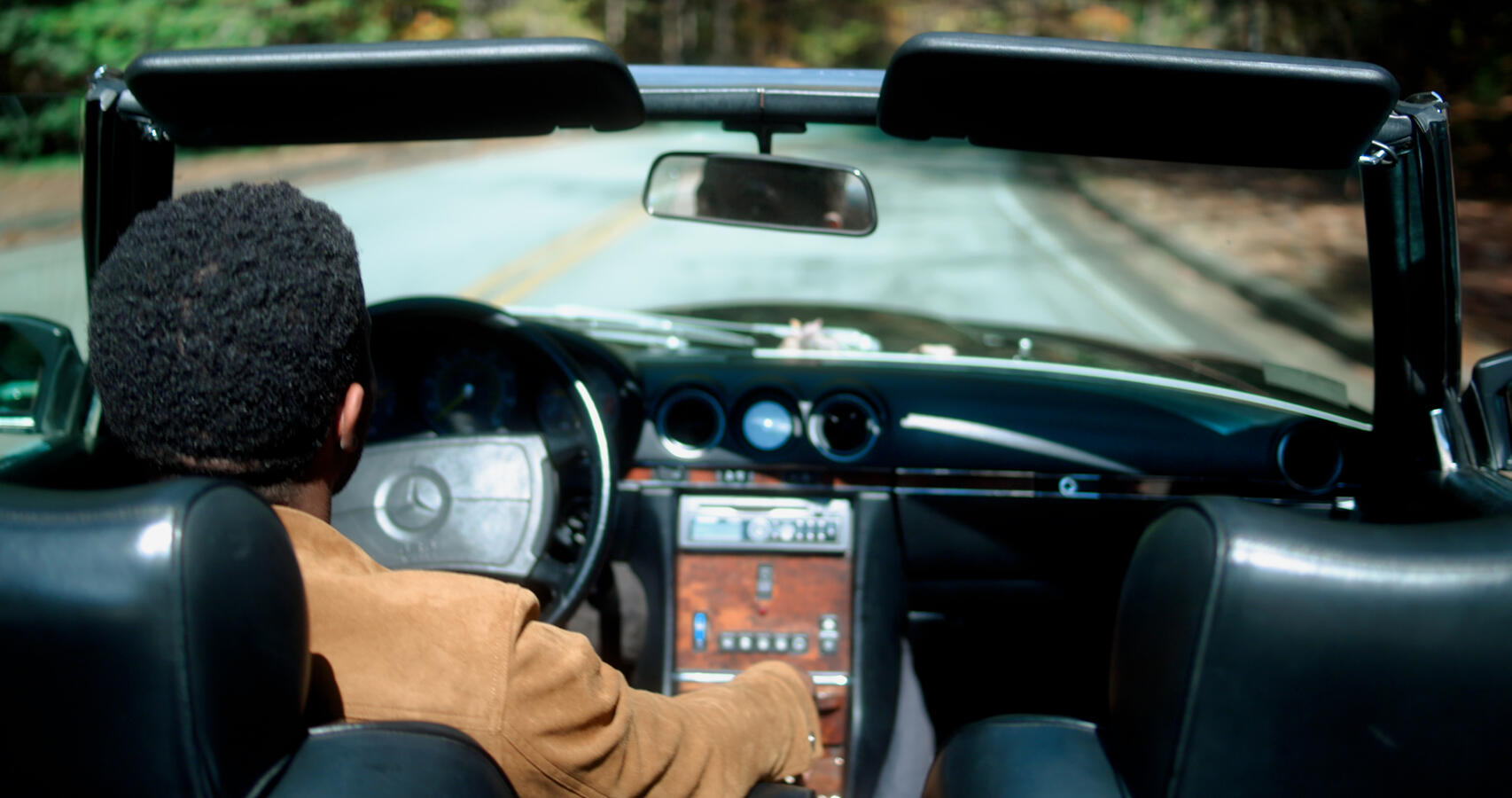 Man drives along sunny road in a Mercedes-Benz 560 SL